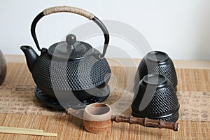 Closeup shot of a cast-iron Japanese teapot, teacups and wooden ladle