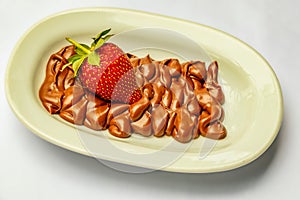 Closeup shot of cocoa cream and single red strawberry on beige plate on white surface