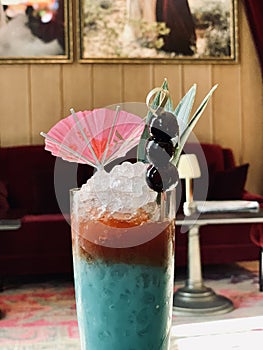 Closeup shot of a colorful beverage with a pink umbrella, cherries on a stick, and some leaves in it