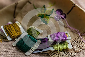 Closeup shot of colorful yarn rolls on a piece of fabric with cross-stitch art of purple grapes