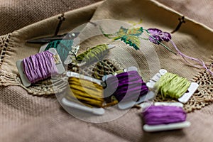 Closeup shot of colorful yarn rolls on a piece of fabric with cross-stitch art of purple grapes