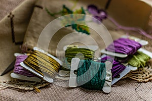 Closeup shot of colorful yarn rolls on a piece of fabric with cross-stitch art of purple grapes