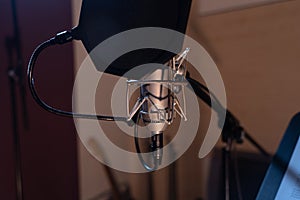 Closeup shot of a condenser microphone with a pop filter and a blurred background