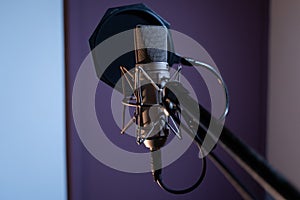 Closeup shot of a condenser microphone with a pop filter and a blurred background