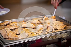 Closeup shot of cooked meat piled in a chafing dish being served from a buffet table