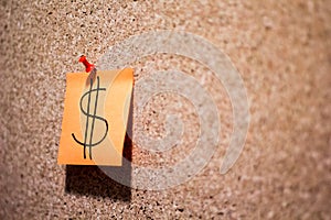 Closeup shot of a cork board with a note of a dollar sign pinned on it