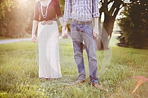 Closeup shot of a couple holding hands on a grassy field with the sun shining above their head