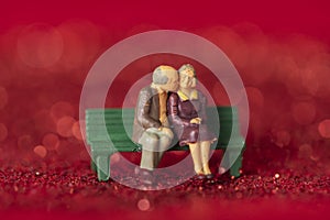 Closeup shot of a couple of old figurines sitting on a bench on red glitter background