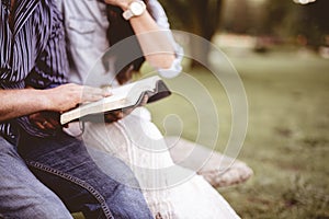 Closeup shot of a couple sitting in the park and reading the bible with a blurred background