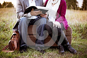 Closeup shot of a couple sitting on a suitcase while reading the bible with a blurred background