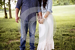 Closeup shot of couple standing in a grassy field while holding hands with a blurred background