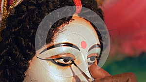 Closeup shot of a craftsman`s hand painting eyes of Goddess Durga`s clay