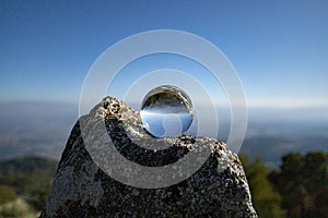 Closeup shot of a crystal ball on the rock with reflections of the sky and the rocks