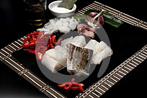 Closeup shot of cut-up fish, peppers, garlic, onion on a cutting board near salt and oil