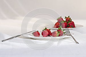 Closeup shot of delicious fresh strawberries with fork and diner knife on a white plate