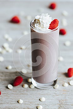 Closeup shot of a delicious strawberry milkshake in a tall glass cup surrounded by strawberries