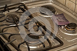 Closeup shot of a dirty gas stove with a sponge in the kitchen