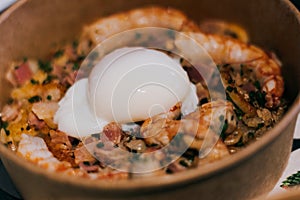 Closeup shot of a dish with undercooked egg with prawns and bacon