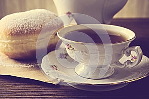 Closeup shot of donut with cup of tea on table in old-fashioned