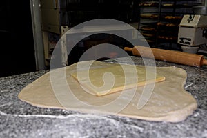 Closeup shot of dough and butter on top and a wooden rolling pin on the table in a bakery