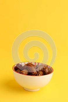 Closeup shot of dry dates fruit in a bowl on a yellow background