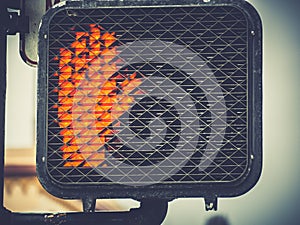 Closeup shot of an electric crosswalk sign with red hand signalling to stop walking