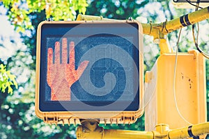 Closeup shot of an electric crosswalk sign with red hand signalling to stop walking