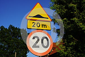 Closeup shot of European road signs for a bump with speed limit against trees and blue sky