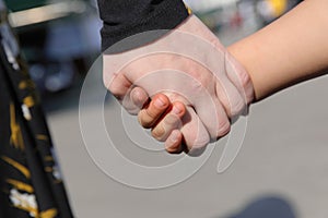 Closeup shot of father and son holding hands in the street on a sunny day