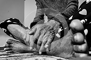 A closeup shot of feet and hands of an elderly woman in India in black and white