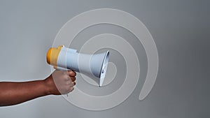 Closeup shot of female hand holding megaphone isolated over gray background