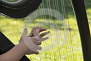 Closeup shot of a female's hands playing the harp on a grass-covered field