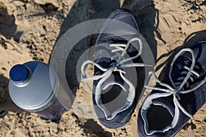 Closeup shot of female sneakers and water bottle standing on a sand