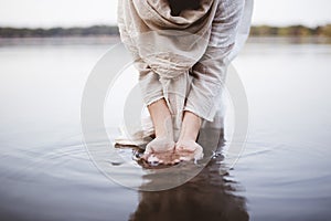 Closeup shot of a female wearing a biblical robe standing in the water while washing her hands