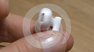 Closeup shot of fingers inspecting soiled white earbud on a wooden background.