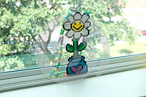 Closeup shot of a flower in a vase made from Kandi beads on a sliding window