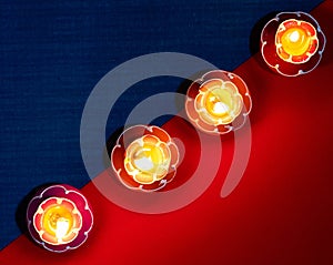 Closeup shot of four flower-shaped burning candles in a diagonal row on a red and blue surface
