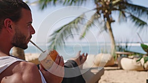 Closeup shot of fresh king coconuts with exotic background. Tourists holding two cocnuts with straws, clink them and