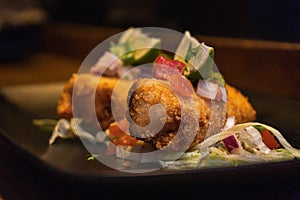 Closeup shot of fried mozzarella sticks with lime and salad in a black plate on the table