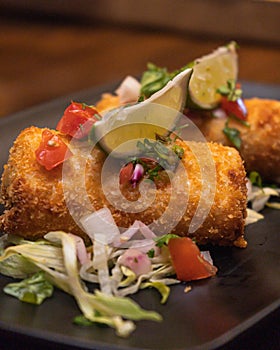 Closeup shot of fried mozzarella sticks with lime and salad in a black plate on the table
