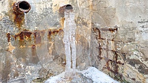 a closeup shot of a frozen water flowing through tube on the street. Big icicle, extreme cold weather