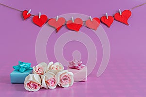 Closeup shot of gift boxes with roses and red love hearts pinned on the rope. Valentine card idea