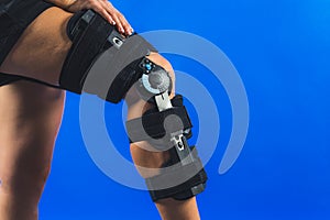 closeup shot of a girl putting her hand on a protective band on her knee injury, trauma and rehabilitation concept, blue