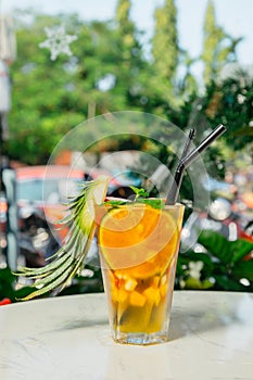 Closeup shot of a glass of cocktail with oranges and min leaves on a white table