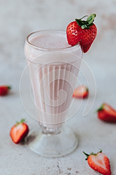 Closeup shot of a glass of strawberry milkshake, with blurred strawberries in the background