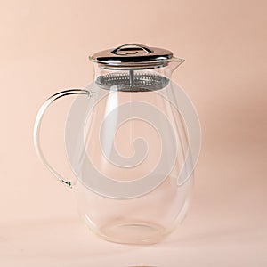 Closeup shot of a glass teapot with a silver strainer on a light pink background