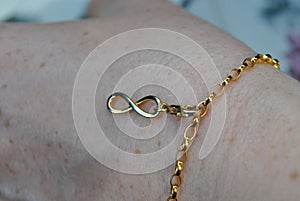 Closeup shot of a golden bracelet with an infinity charm