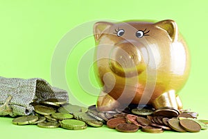 Closeup shot of a golden piggy bank, and coins falling out of a tiny sack on a green background