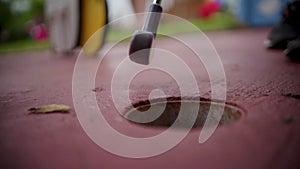 Closeup shot of a golf club pushing a golf ball into a minigolf hole