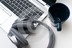 Closeup shot of a gray headphone on a gray laptop next to a blue mug isolated on a white background